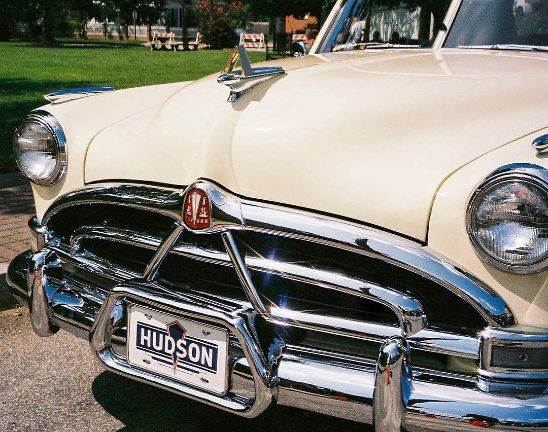 Auto-generated description: A vintage cream-colored Hudson car with chrome detailing is parked in a sunny outdoor setting.
