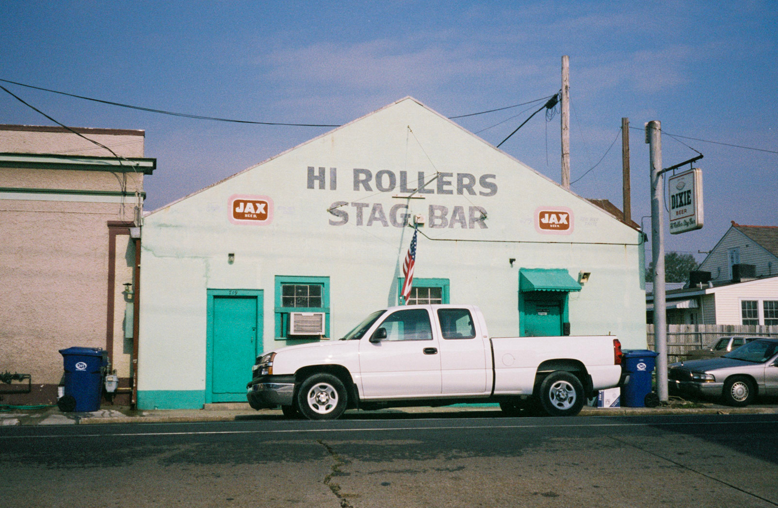 Auto-generated description: A white truck is parked in front of a light green building labeled Hi Rollers Stag Bar.