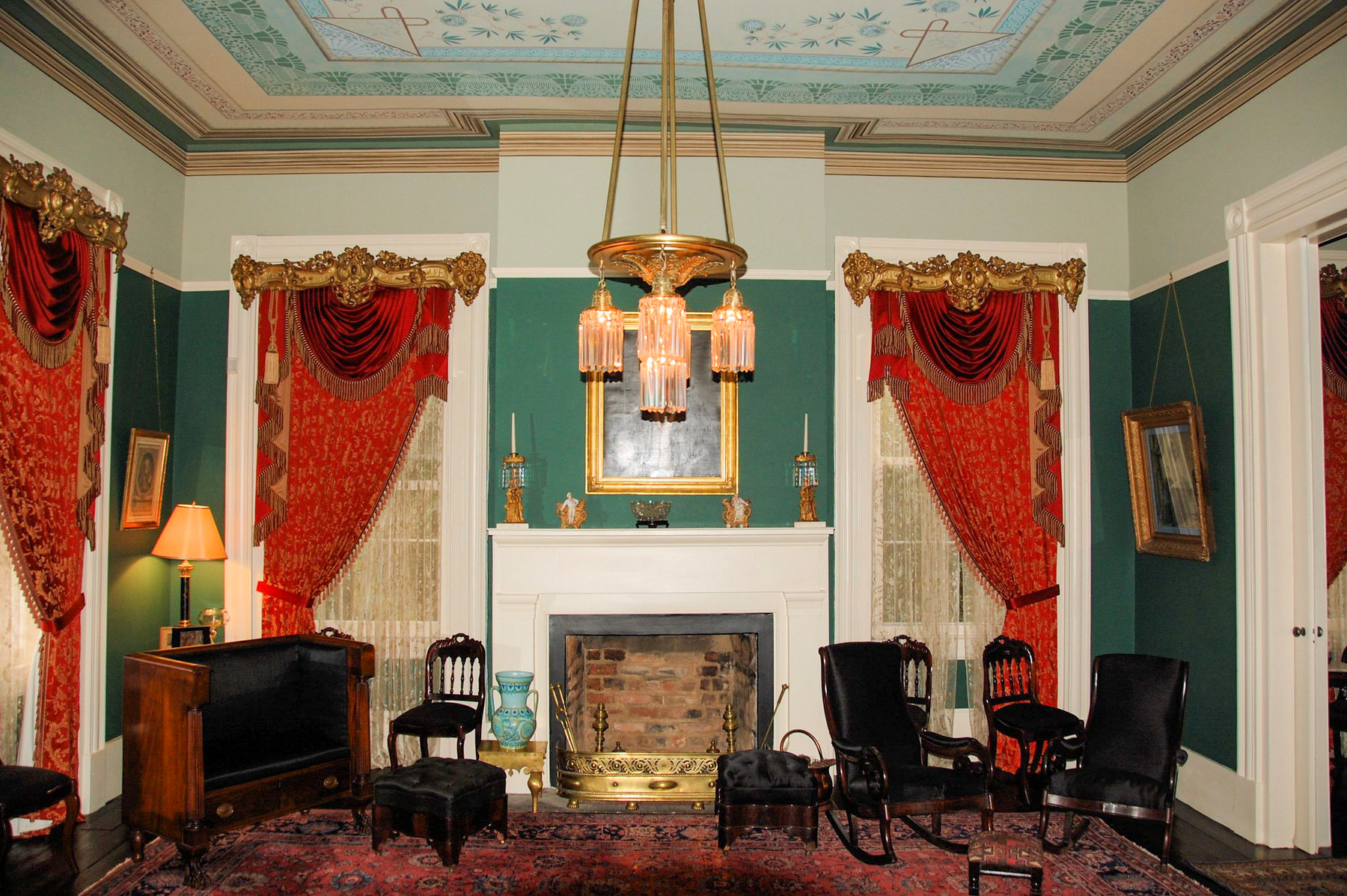 Auto-generated description: A richly decorated room features an ornate fireplace, elegant drapery, and antique furniture with a vintage chandelier above.