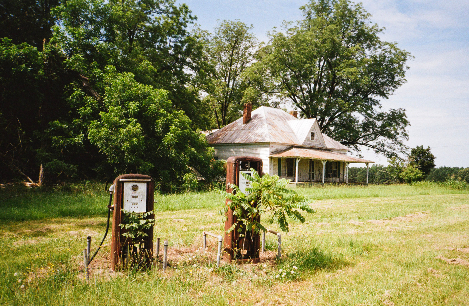 Auto-generated description: An old, overgrown gas station stands in front of a rustic house surrounded by trees and greenery.