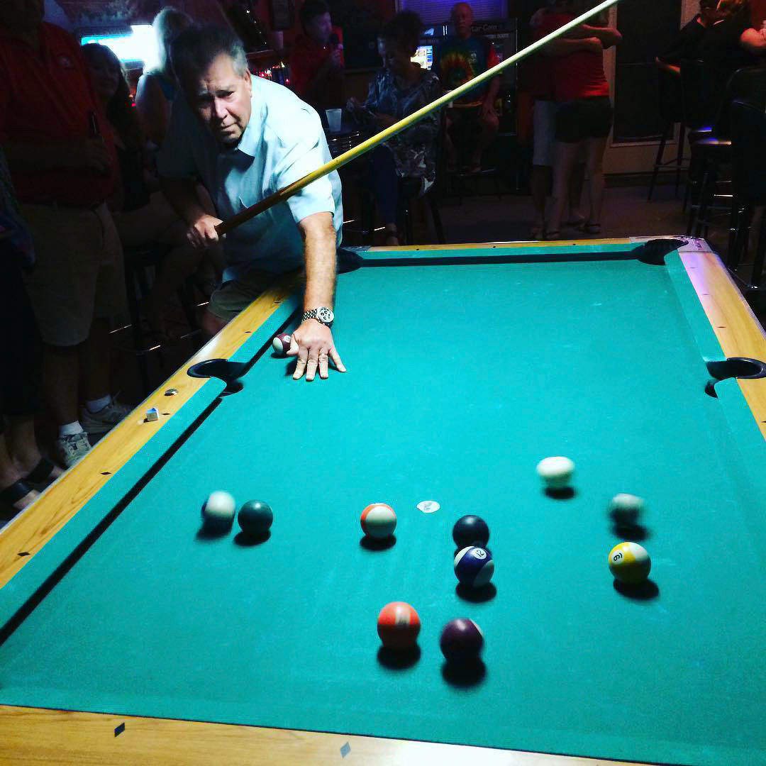 Auto-generated description: A man leans over a pool table, concentrating on taking a shot as the colorful balls are in motion.