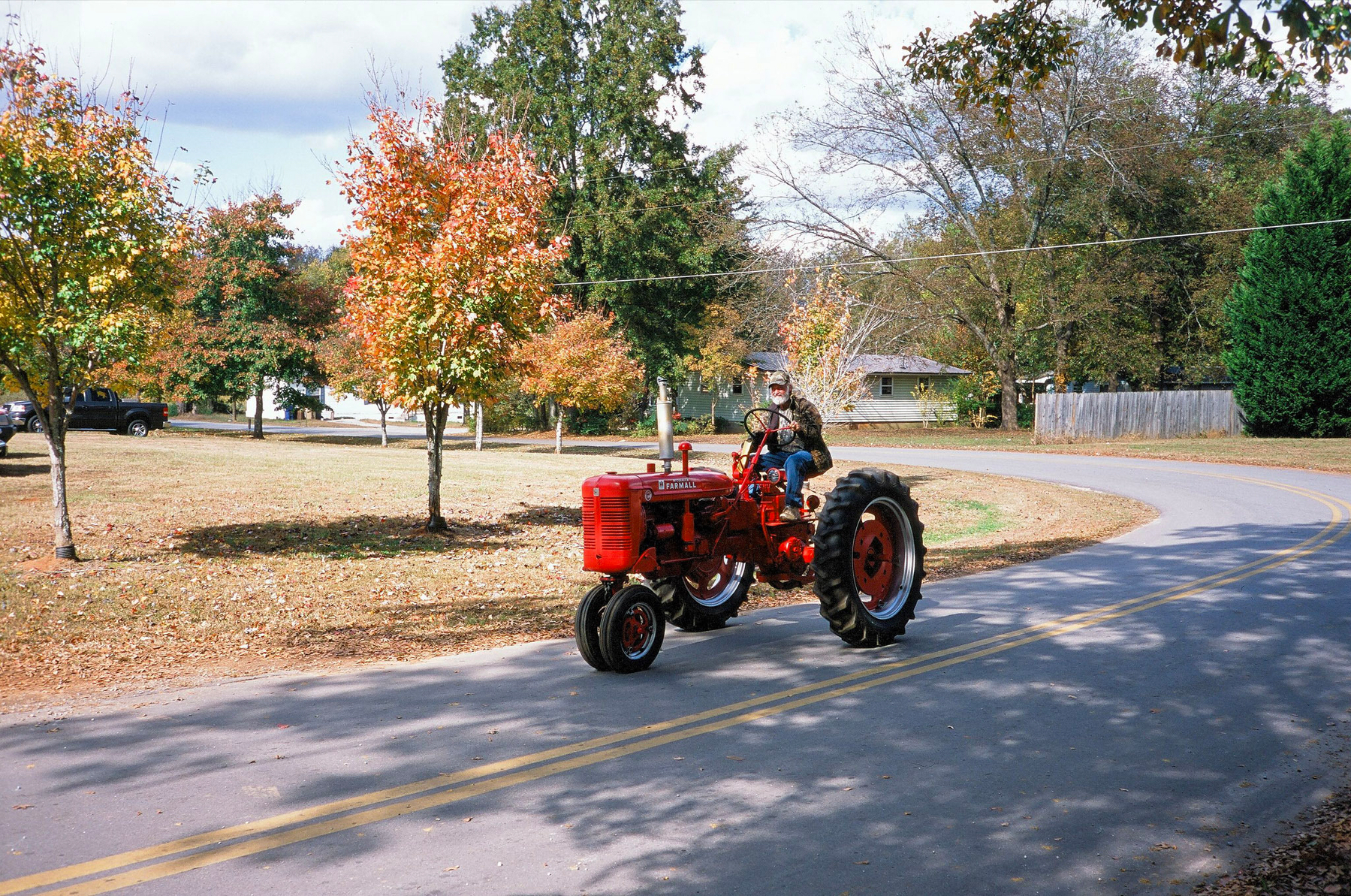 Auto-generated description: A person is driving a red tractor on a tree-lined street during autumn.
