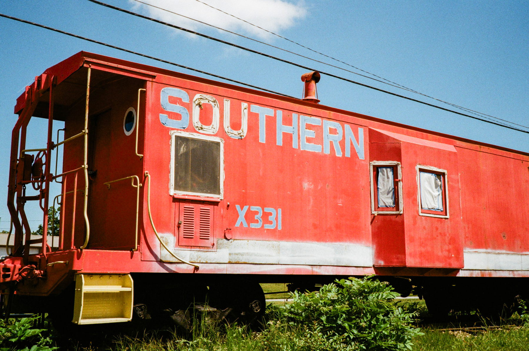 Auto-generated description: A red caboose labeled SOUTHERN X331 is situated on railway tracks surrounded by greenery under a blue sky.