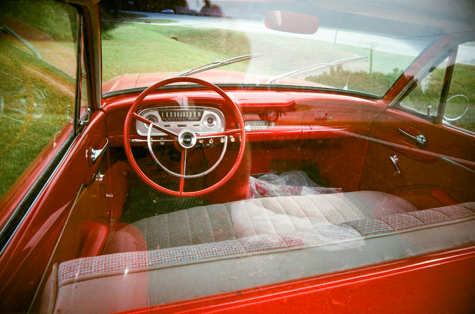 Auto-generated description: A vintage car interior features a bright red dashboard and steering wheel, viewed through the window.